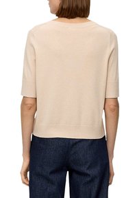 Pullover corto a maniche corte color beige chiaro con vestibilità rilassata, texture lavorata a maglia e orlo a costine, abbinato a pantaloni in denim scuri.