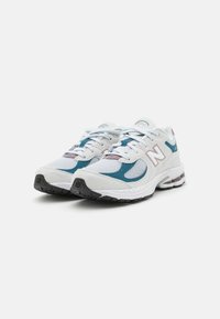 Baskets de sport blanches avec des accents teal et mauve, en maille et en daim, lacets ronds et semelle rembourrée.