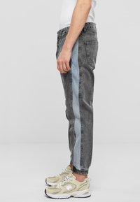 Joggers de mezclilla gris con franjas laterales en azul claro, ajuste tapered, cintura elástica y puños. Combinados con zapatillas beige.
