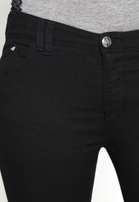 Černé džíny vyrobené z denimu, s úzkým střihem, zapínáním na knoflík, přední kapsou a decentním logem na kapse.