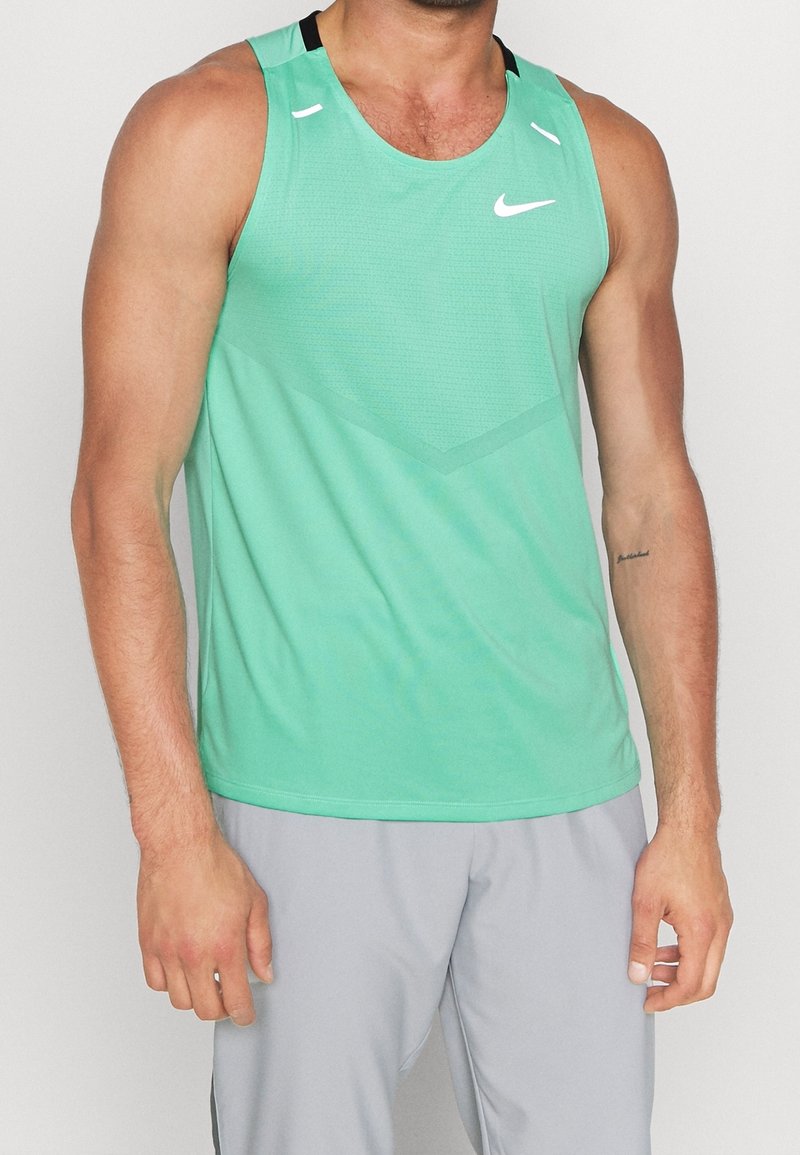 Homme portant un maillot de sport Nike vert sans manches et un short de sport gris clair sur un fond uni.