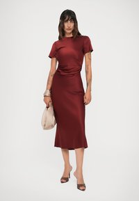 Abito in satin bordeaux con maniche corte e vita drappeggiata, che presenta una silhouette aderente e una lunghezza midi. Completato da una borsa neutra.