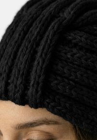 Sort strikket hue med et tekstureret mønster, der har tykke fletninger. Materialet virker blødt og varmt, velegnet til koldt vejr.