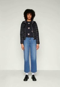 Giubbotto imbottito nero, maglione a maniche lunghe blu navy con motivi a cuore rosa chiaro, jeans a zampa d'elefante blu chiaro e scarpe nere con lacci.