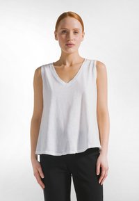 Top blanco sin mangas con diseño de cuello en V y ajuste holgado. Hecho de tela ligera con una superficie ligeramente texturizada.