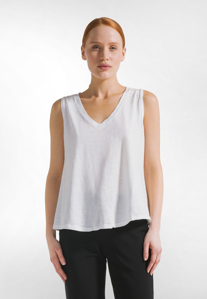 Top blanco sin mangas con diseño de cuello en V y ajuste holgado. Hecho de tela ligera con una superficie ligeramente texturizada.