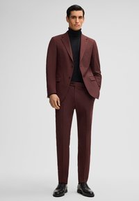 Bordeaux op maat gemaakt pak met een enkelvoudige blazer, zwarte coltrui en zwarte leren schoenen. Glenzachtige textuur, moderne pasvorm en strakke lijnen.