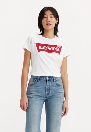 Witte katoenen t-shirt met een groot rood Levi's-logo, gecombineerd met hoog uitgesneden blauwe spijkerbroeken die een ontspannen pasvorm tonen.