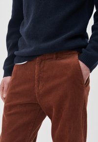 Pantaloni din corduroy maro cu textură verticală, asociați cu un pulover din tricot bleumarin. Buzunare vizibile, croială relaxată.