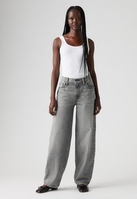 Gray wide-leg jeans with a high waist and five pockets, paired with a fitted white tank top. Material appears denim with a soft texture.