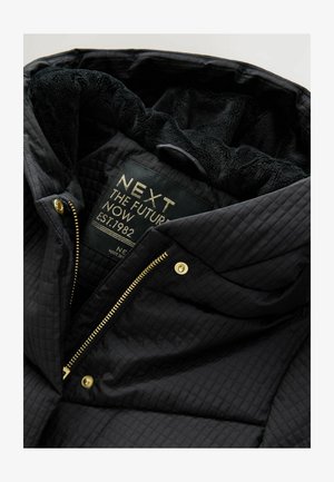 Černá prošívaná bunda s měkkým černým kožíškem uvnitř. Obsahuje zlatý zip a cvokové knoflíky. Na štítku je uvedeno jméno značky a rok založení.