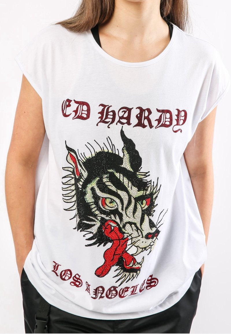 Camiseta de algodón blanca con mangas cortas que presenta un gráfico de tigre negro y rojo adornado con piedras de strass, texto "ED HARDY" arriba y "LOS ÁNGELES" abajo.