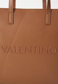 Barna textúrájú táska a fronton reliefszerű "VALENTINO" logóval, két lapos fogantyúval és struktúrált formával.