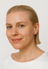 Boucle d'oreille géométrique en argent présentée sur un modèle avec des cheveux blonds courts et lissés en arrière, portant un haut blanc sur un fond neutre.