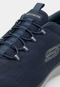 Navy blue mesh sneaker with molded details, elastic lacing system, and a gray logo on the side. Textured surface with a lightweight design.
