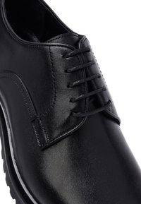 Zapato de vestir de cuero negro con cordones cerrados, detalles de costura y acabado pulido suave.