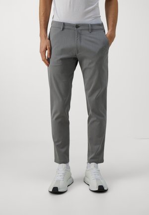 Pantaloni grigi su misura con finitura texturizzata, dotati di chiusura con bottone e passanti per cintura, abbinati a scarpe da ginnastica bianche.