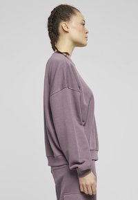 Överdimensionerad sweatshirt i dammig lila, tillverkad av mjuk bomull. Har långa ärmar, rund halsringning och ribbade muddar. Slät textur.