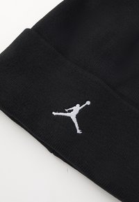 Beanie en tricot noir avec un logo Jumpman brodé en blanc. Le tissu semble doux, avec une texture lisse et un design ajusté.