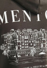 Dunkelbrauner Hoodie mit einem weißen Grafikdesign einer Küstenstadtlandschaft, mit detaillierten Gebäuden, Palmen und einem Segelboot im Vordergrund.