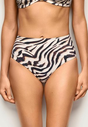 Kobieta nosząca bikini z wysokim stanem z abstrakcyjnym wzorem zebry w kolorach czarnym, białym i brązowym, ręce luźno opuszczone wzdłuż ciała na jednolitym tle.