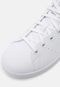 Vit sneaker med ovandel i slät läder, rund tå, platta bomullssnören och sex ögla-hål, med en minimalistisk design.