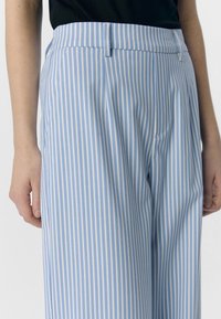 Pantaloni a righe blu chiaro e bianchi con vita alta, caratterizzati da pieghe e tasche laterali. Realizzati in un tessuto morbido con una vestibilità tailored.