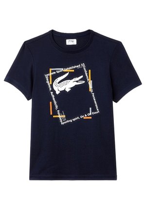 Granatowy t-shirt z krótkim rękawem z białym logo krokodyla umieszczonym na środku pochylonej kwadratowej ramki z pomarańczowo-białym tekstem.