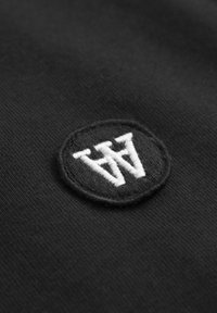 Tissu noir avec un petit patch circulaire noir brodé de lettres "W" blanches superposées au centre.