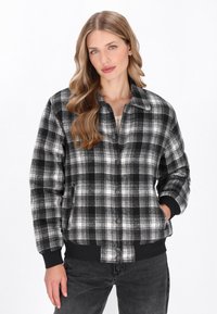 Fekete-fehér kockás dzseki, galléros nyakkal, gombos záródással, oldalsó zsebekkel és bordás mandzsettával és szegéllyel. Puha anyagból készült.