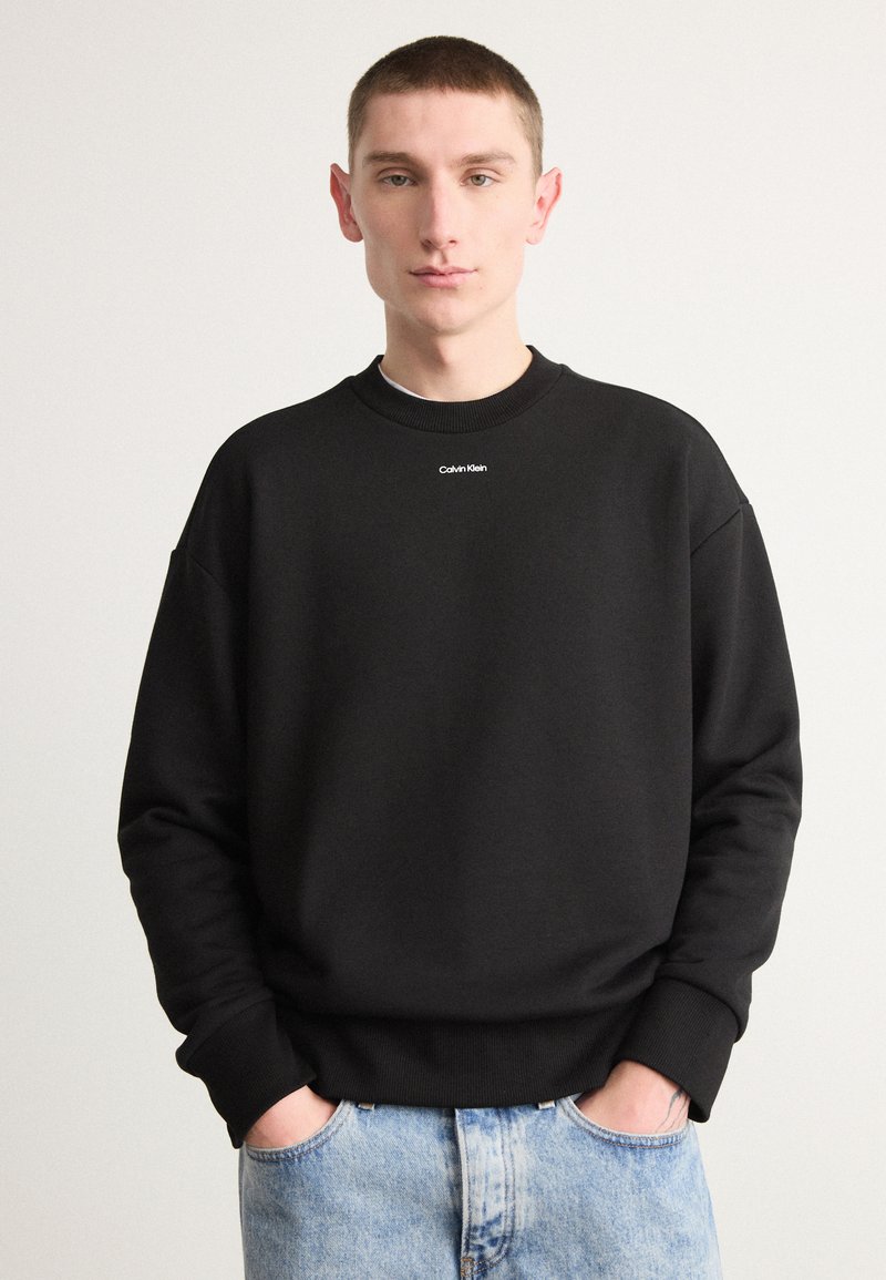 Sudadera negra hecha de una mezcla de algodón con puños y cuello acanalados. Presenta un pequeño logo blanco de "Calvin Klein" en el pecho.
