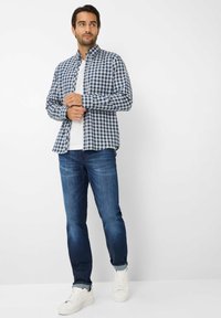 Blauw en wit geblokt overhemde, lange mouwen, gedragen over een wit t-shirt, gecombineerd met blauwe jeans en witte sneakers.
