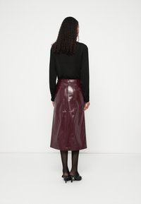 Μίντι φούστα σε μπορντό χρώμα, ψηλόμεση από δερματίνη με γυαλιστερό φινίρισμα, που διαθέτει φερμου�άρ στο πίσω μέρος και ραφές λεπτομέρειας, συνδυασμένη με μαύρο μπλουζάκι μακρυμάνικο.