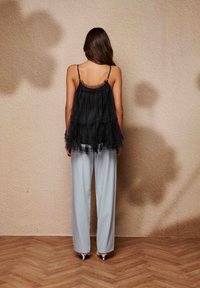 Μαύρο τοπ από στρωματοποιημένο τούλι με ρυθμιζόμενους ιμάντες, συνδυασμένο με ανοιχτό μπλε παντελόνι με φαρδιά μπατζάκια και λευκά παπούτσια με τακούνι. Υπόβαθρο με υφή.