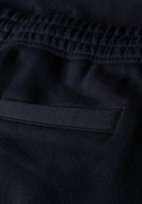 Gros plan sur un pantalon en tissu noir avec une ceinture élastique et une poche passepoilée horizontale.