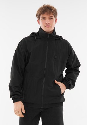 Black waterproof jacket with a zip front, adjustable hood, elastic cuffs, and two side pockets. Made of lightweight, textured fabric.