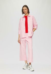 Roze denimjasje en bijpassende broek, gecombineerd met een rode gebreide top. Sneakers zijn grijs met witte accenten. Eenvoudige, casual outfit.