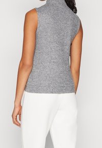 Mouwloos grijs coltruitje van zachte gebreide stof, met een geribde zoom en een gladde textuur, gecombineerd met witte broek.