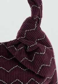 Sac à main en velours côtelé couleur prune foncée avec un motif texturé en zigzag. Orné de clous carrés argentés le long des coutures. Détail de poignée nouée.