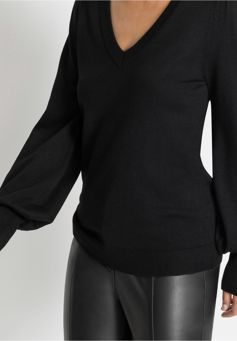 Pull en tricot noir avec col en V, manches larges et ourlet côtelé, associé à un pantalon en cuir noir. Texture lisse, sans motifs ni accents.