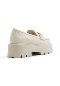 Beige platform loafers met een glad leren buitenkant, ronde voorkant, decoratieve band en een getextureerde rubberen zool met een diep profiel.