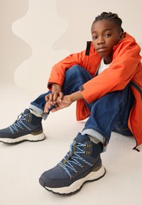 Mørkeblå vandrestøvler med lyseblå snørebånd og grønne detaljer. Har høj skaft, gummisål og polstret krave for komfort.