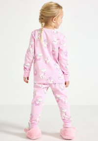 Rosa pyjamaset med enhörningsmönster, långärmad tröja och byxor, tillverkad av mjukt tyg. Matchas med fluffiga rosa tofflor.