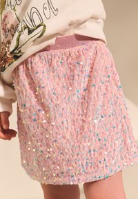 Jupe rose ornée de sequins, avec une taille froncée, un tissu texturé et un effet scintillant grâce aux sequins irisés répartis sur toute la surface.