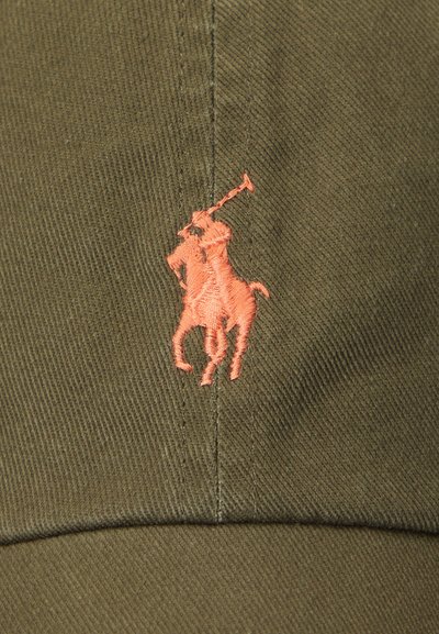 Olivově zelená látka s oranžovým vyšitým logem osoby hrající polo na koni, přišitá podél švu.