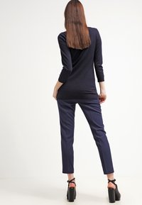 Marinblå långärmad tröja med en åtsittande design och rundad rygg, som matchas med skräddarsydda marinblå byxor och svarta klacksandaler.