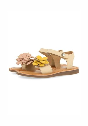 Sandalias beige con acentos florales en rosa y amarillo, con una parte superior de cuero suave, correa ajustable y suela plana.