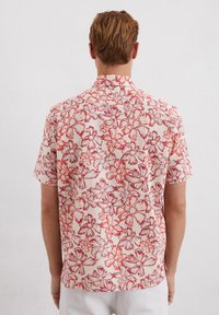 Kortarmpoloshirt in crème met een rode bloemprint, met een klassieke kraag en een losse pasvorm. Zacht, lichtgewicht materiaal verhoogt het comfort.