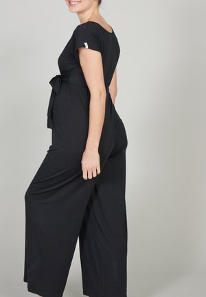Schwarzer Jumpsuit mit kurzen Ärmeln und einem Bindegürtel in der Taille. Fließendes, weites Beindesign, weicher Stoff und ein rund ausgeschnittenes Rückendetail.