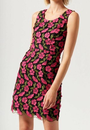 Robe noire sans manches avec broderie florale rose et feuilles vertes, taille cintrée, portée par une personne debout avec une main posée naturellement.